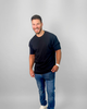 Man wearing a black t-shirt and blue jeans on a gray background